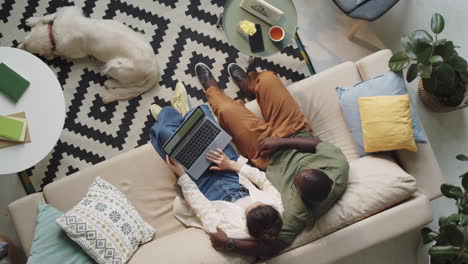 Family-Couple-Using-Laptop-and-Speaking-on-Sofa-at-Home